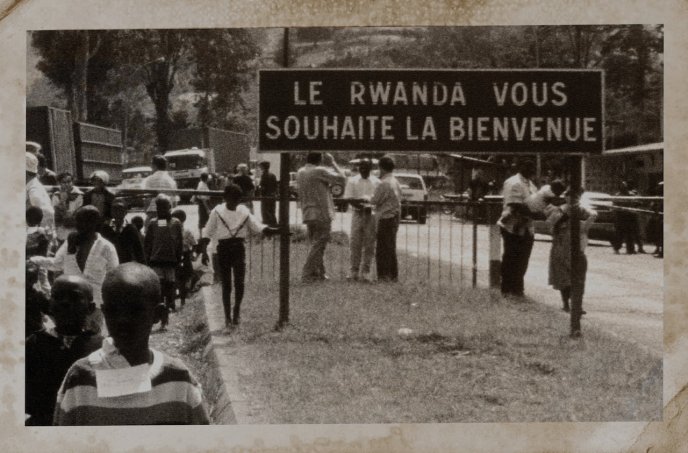 Photographie en noir et blanc avec personnes dans la rue et panneau "Le Rwanda vous souhaite la bienvenue" (Photographie décrite dans le Convoi de Beata Umubyeyi Mairesse, Flammarion, 2024)