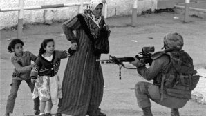 Femme âgée tenant deux fillettes par la main, faisant face à un soldat accroupi pointant une arme