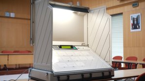 Machine de vote électronique ouverte dans un bureau de vote, avec écran et boutons de sélection visibles.