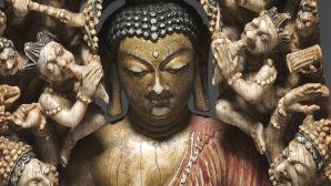 Statue sculptée représentant un Bouddha au visage serein, les yeux clos, entouré de nombreuses petites figures humaines, formant un décor dense et symétrique autour de sa tête et de ses épaules