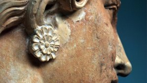 Gros plan du profil d'une sculpture antique en terre cuite, montrant un visage féminin orné d’une boucle d'oreille en forme de rosette