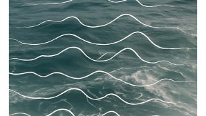 Surface de l’océan vue d’en haut, avec des vagues bleu-vert sur lesquelles sont superposées des lignes blanches ondulées, parallèles, évoquant le mouvement de la mer