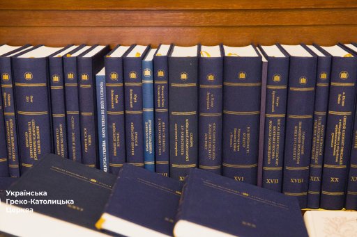 Étagère en bois sur laquelle sont rangés des livres à couverture rigide bleue avec des titres dorés, principalement en ukrainien