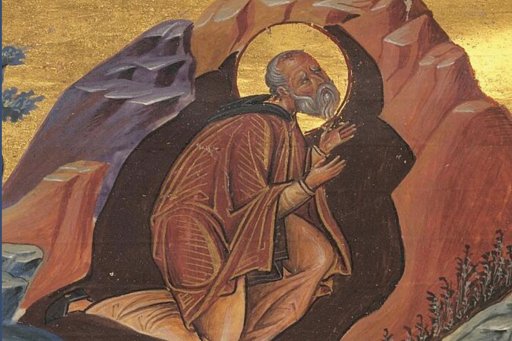 Homme barbu en prière, vêtu d'une robe marron, dans un paysage rocheux