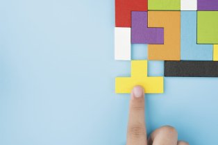 Un doigt positionne la dernière pièce jaune d’un puzzle coloré sur fond bleu.