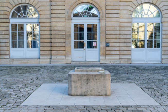 Socle vide en pierre devant un bâtiment avec des portes et fenêtres en arcades
