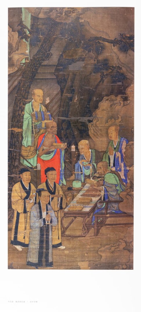 Peinture ancienne représentant des moines en robes colorées autour d’une table avec des rouleaux et des objets