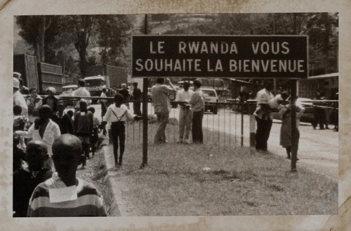 Black and white photograph with people in the street and "Rwanda welcomes you" sign (Photograph described in Convoy by Beata Umubyeyi Mairesse, Flammarion, 2024)