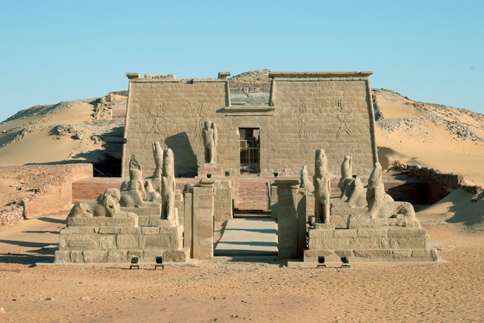 Temple égyptien antique en pierre situé dans le désert, orné de statues et bas-reliefs
