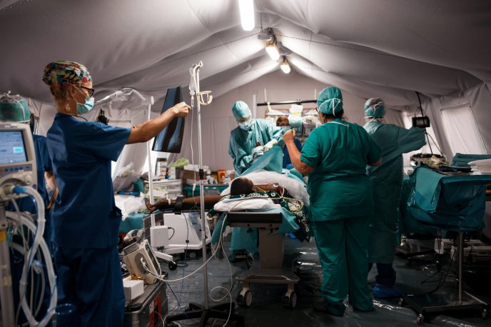 Équipe médicale en opération dans un bloc chirurgical sous tente, avec patient et équipements médicaux.
