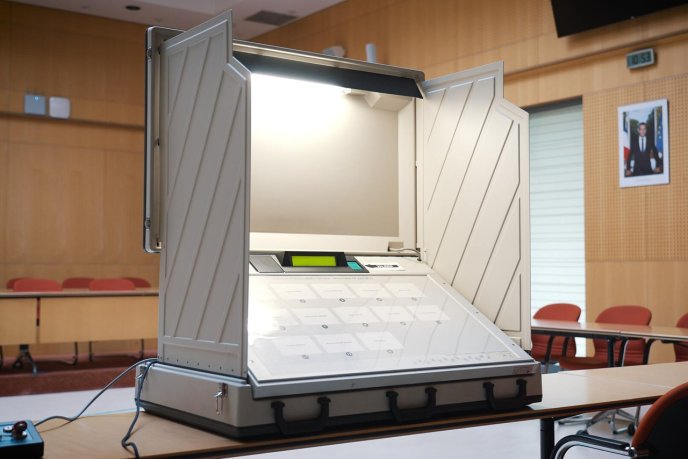 Machine de vote électronique ouverte dans un bureau de vote, avec écran et boutons de sélection visibles.
