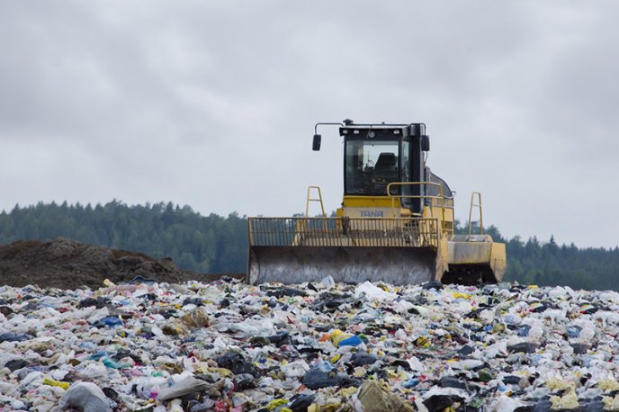 Afficher l'image en plein écran : Bulldozer compactant des déchets dans une décharge à ciel ouvert, sous un ciel nuageux