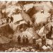 Early sepia photograph of workers in a stone quarry, scattered over boulders with tools and cut stones on the ground.