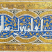 Bandeau décoratif en calligraphie arabe blanche sur fond bleu et or, ornée de motifs végétaux et encadrée de motifs géométriques dorés