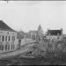 Vue ancienne d’un village avec église, maisons en pierre et fontaine centrale.